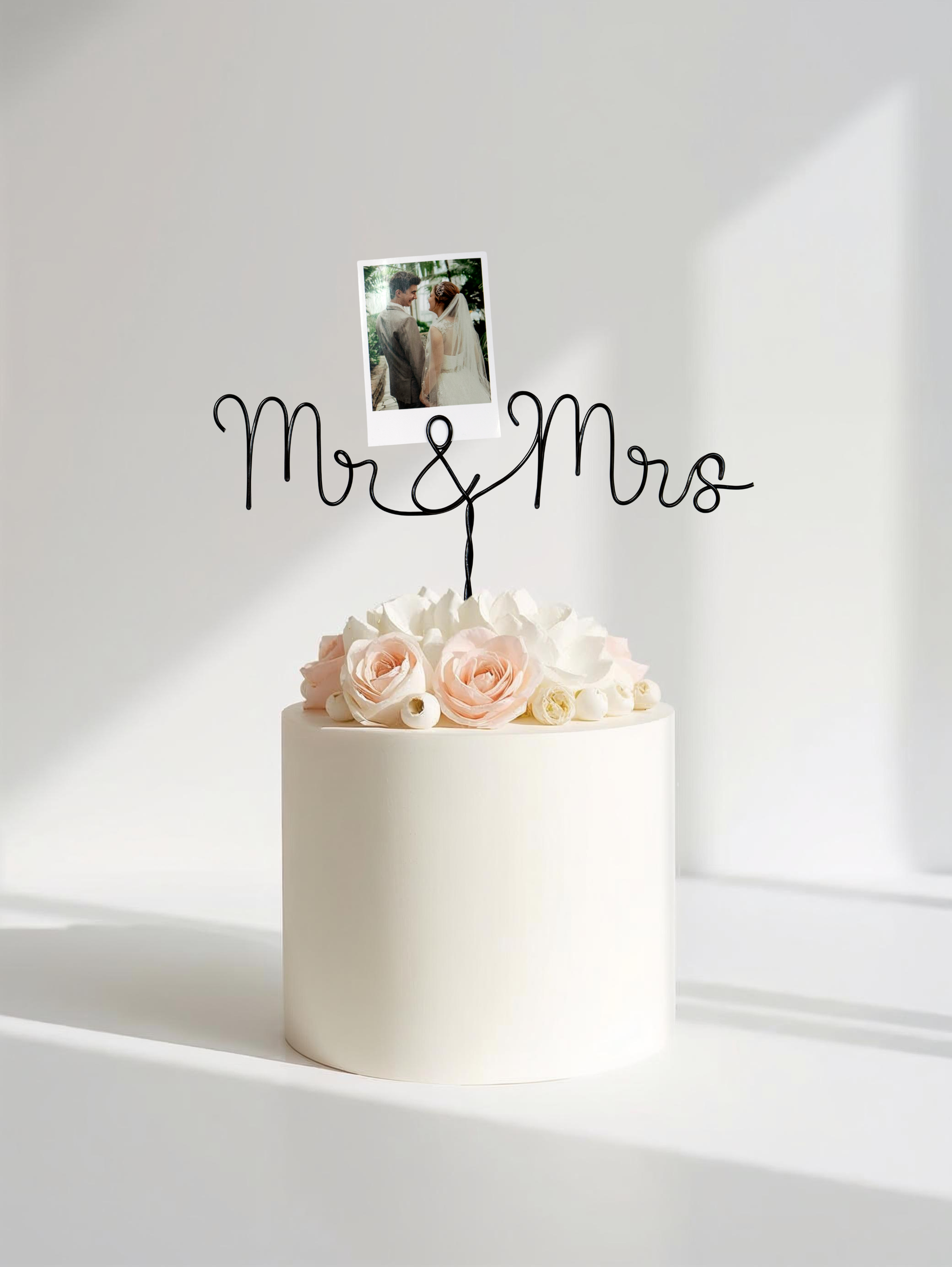 White cake with pink roses and a 'Mr & Mrs' topper on a white background