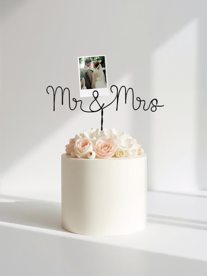 White cake with pink roses and a 'Mr & Mrs' topper on a white background