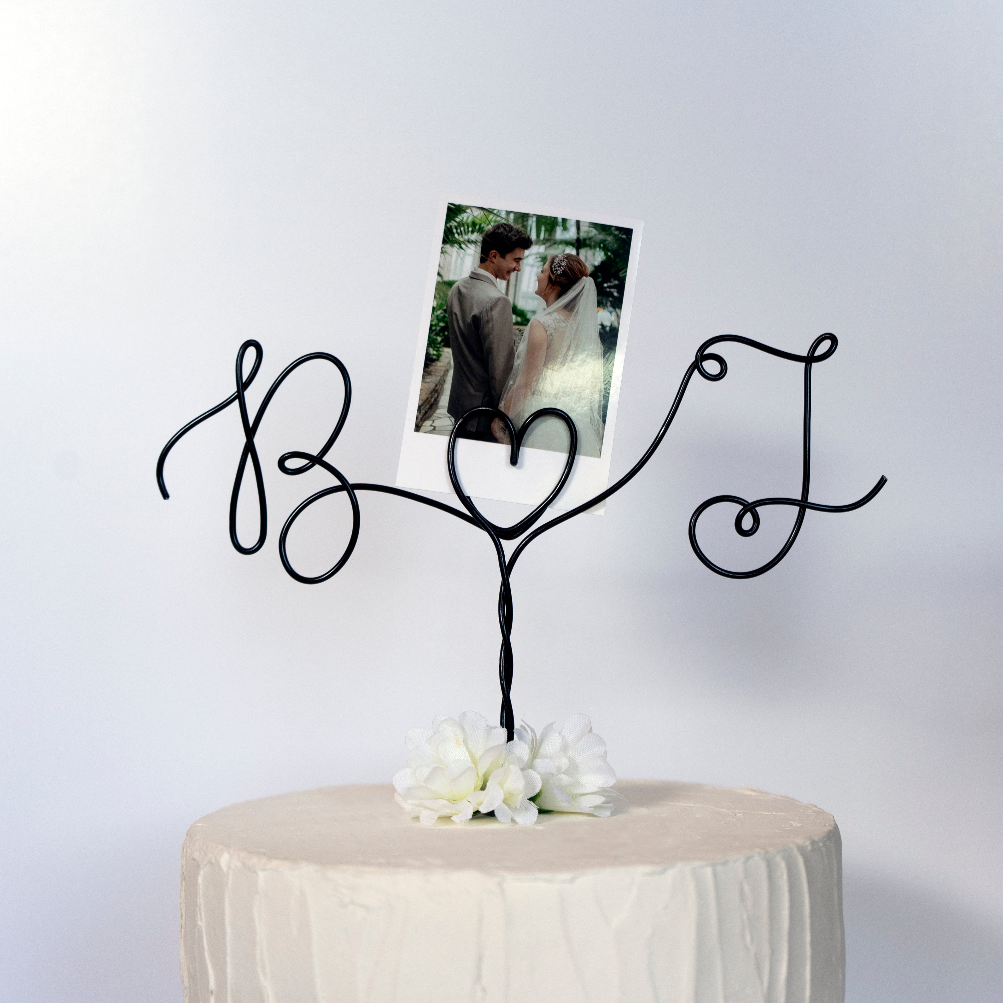 Gold wire cake topper with personalized initials on a cake against a dark background with polaroid photo holder
