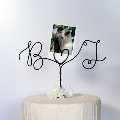 Gold wire cake topper with personalized initials on a cake against a dark background with polaroid photo holder
