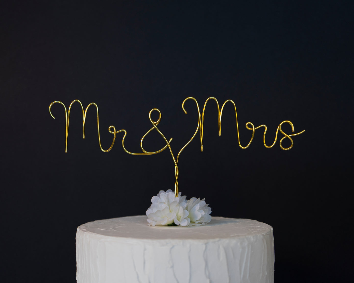 Gold 'Mr & Mrs' cake topper on a white cake against a black background