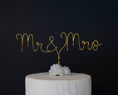 Gold 'Mr & Mrs' cake topper on a white cake against a black background