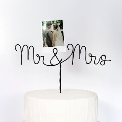 Cake topper with 'Mr & Mrs' on a white cake against a white background