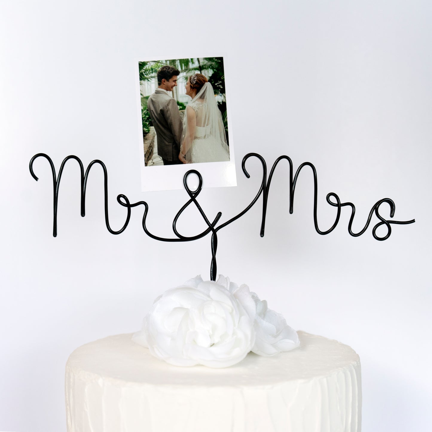 Cake topper with 'Mr & Mrs' on a white surface with a photo of a couple.